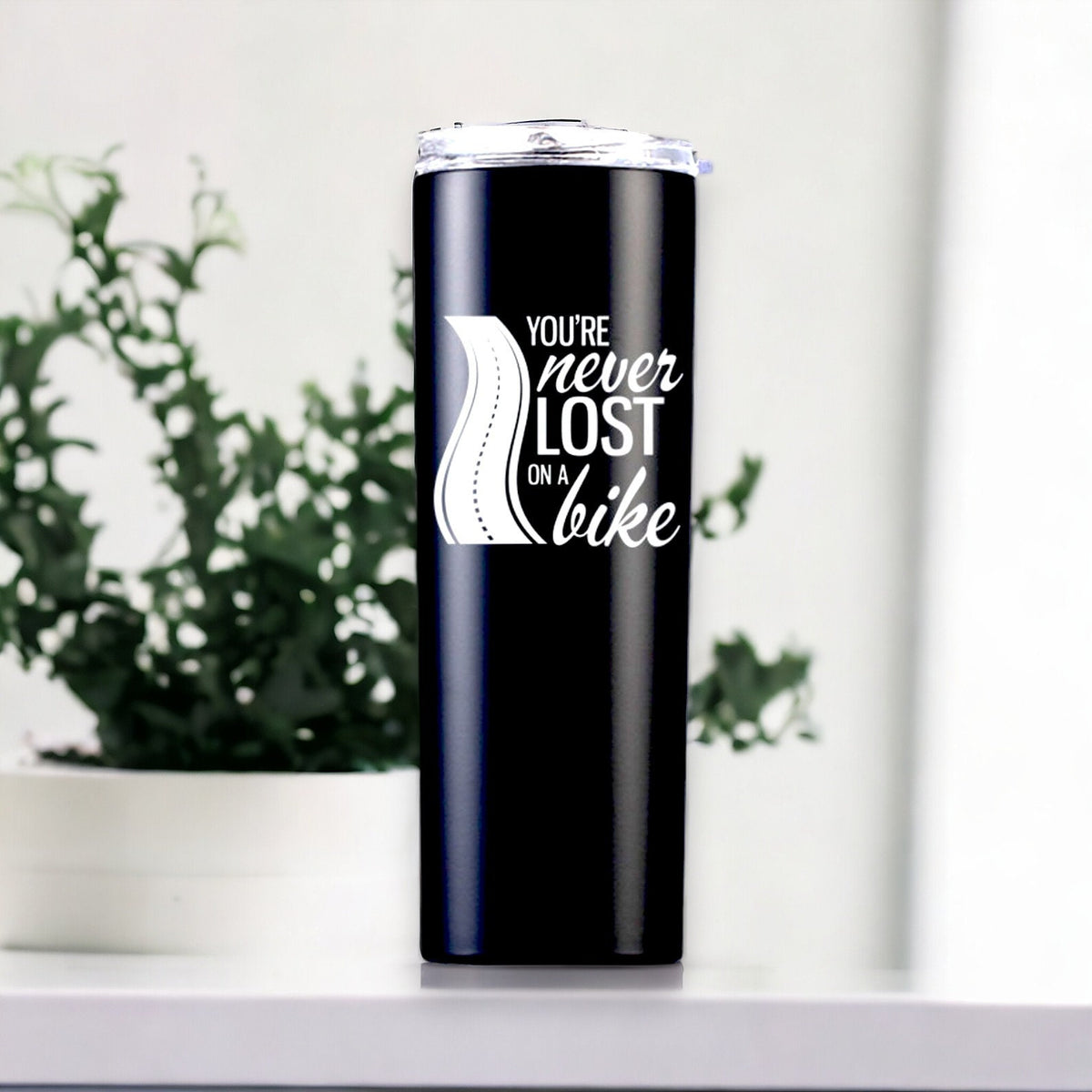 Black personalized motorcycle travel mug on a white shelf with leafy greenery behind it