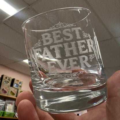 Clear glass with 'Best Father Ever' engraving held in a hand against a tiled ceiling.