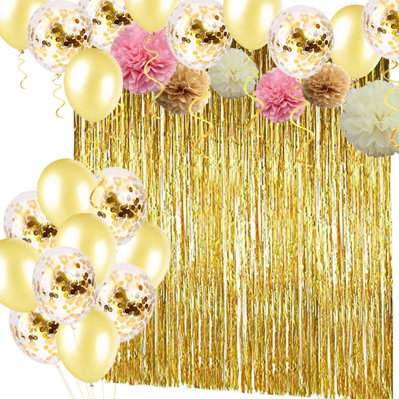 Arrangement of white, gold, and pink paper flower pom-poms next to a spool of gold curling ribbon, ready for party decoration.