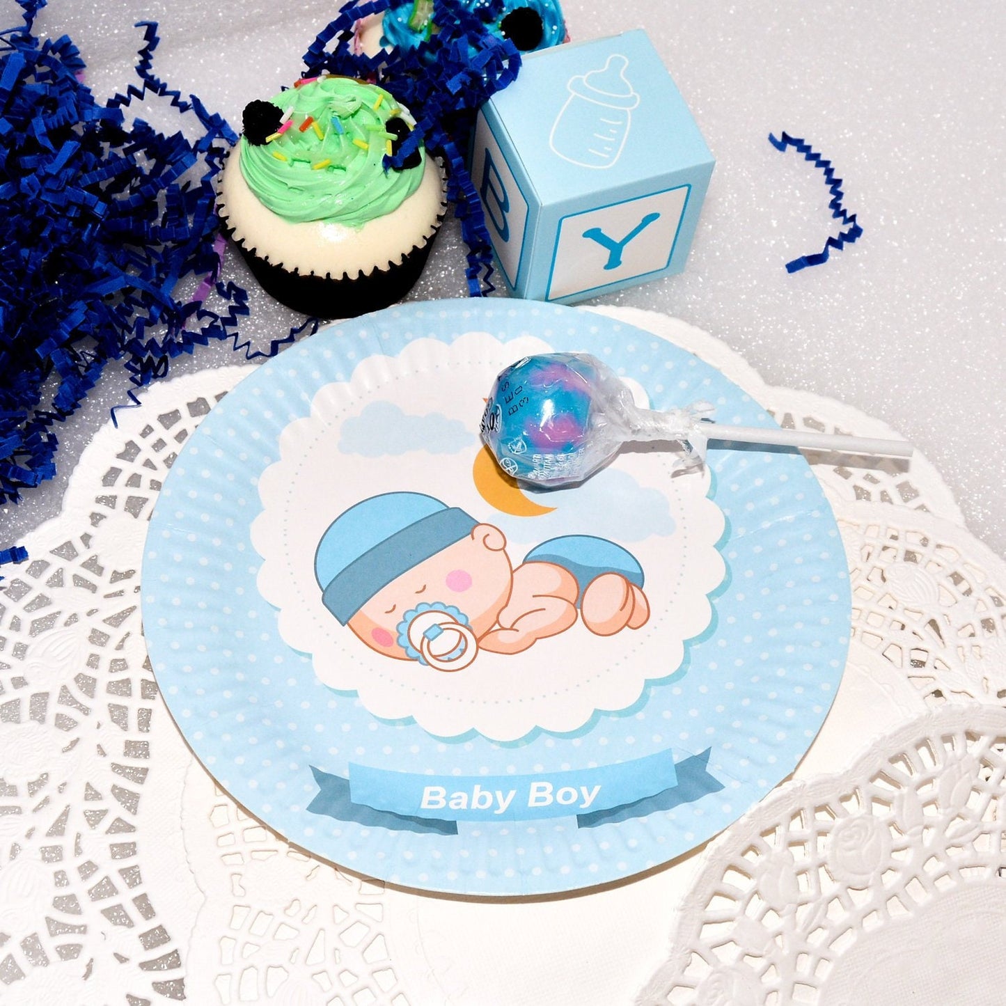 A stack of blue sleeping baby boy dessert plates next to party treats, setting the scene for a celebration.