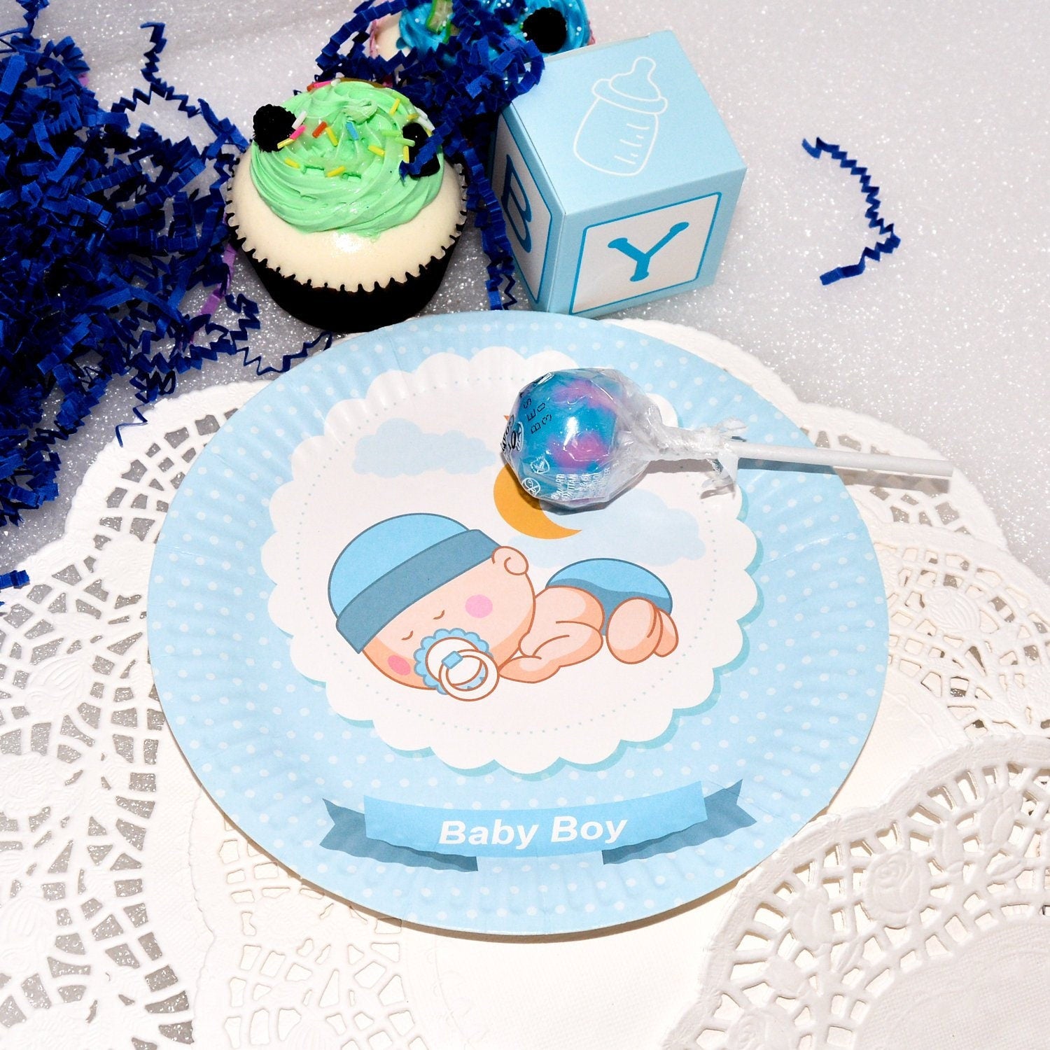 A stack of blue sleeping baby boy dessert plates next to party treats, setting the scene for a celebration.