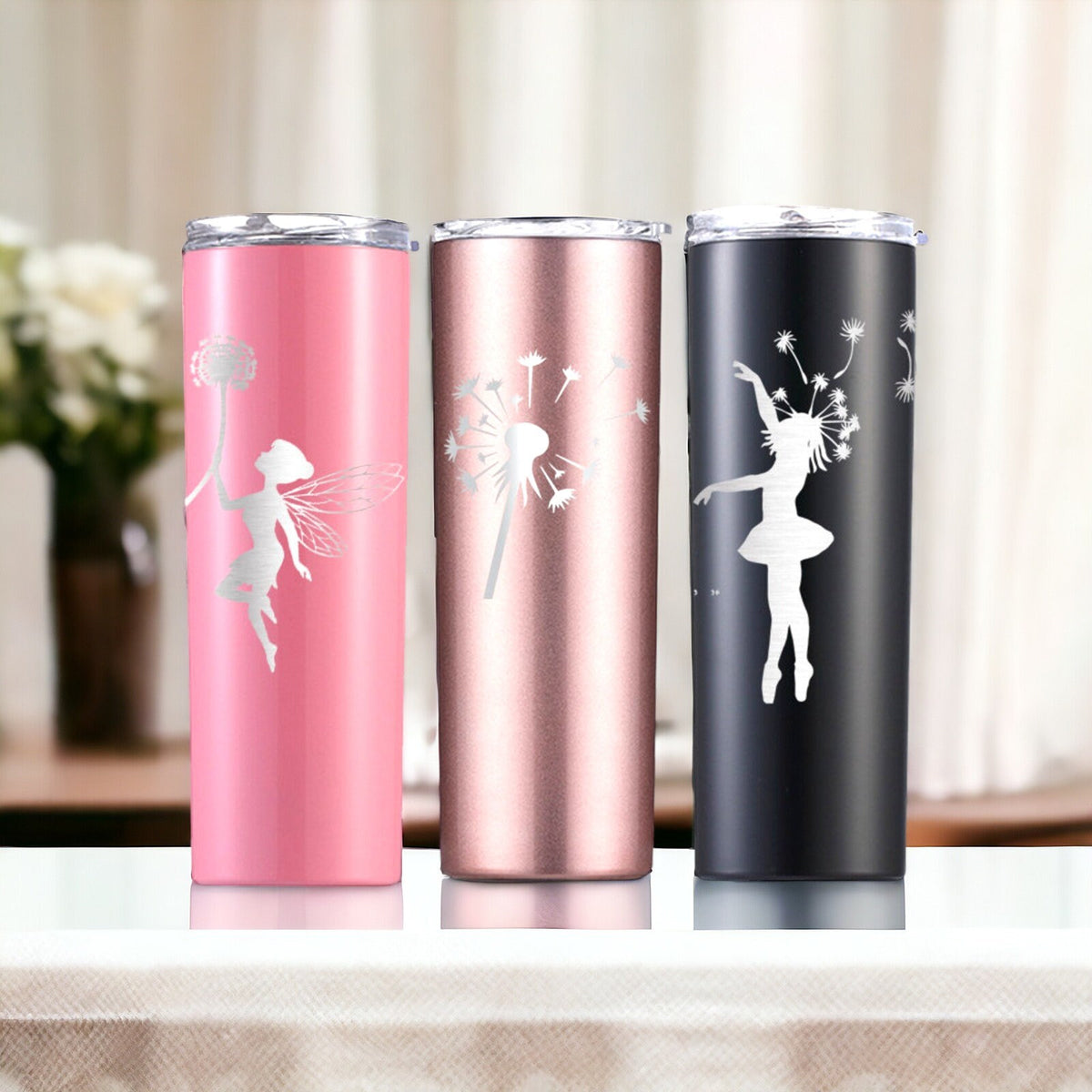 Engraved fairy tumbler group in pink, silver, and black arranged near flowers in a bright setting.