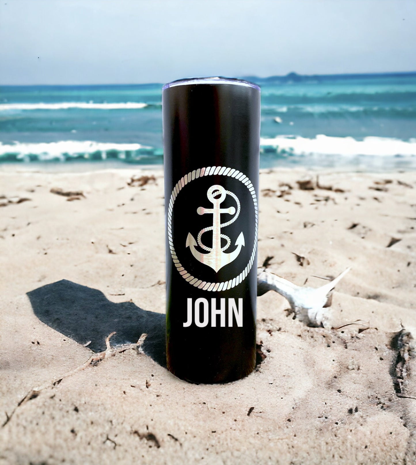 An anchor tumbler with custom laser engraving, shown in a natural setting, possibly on a boat or near water, for scale and context.