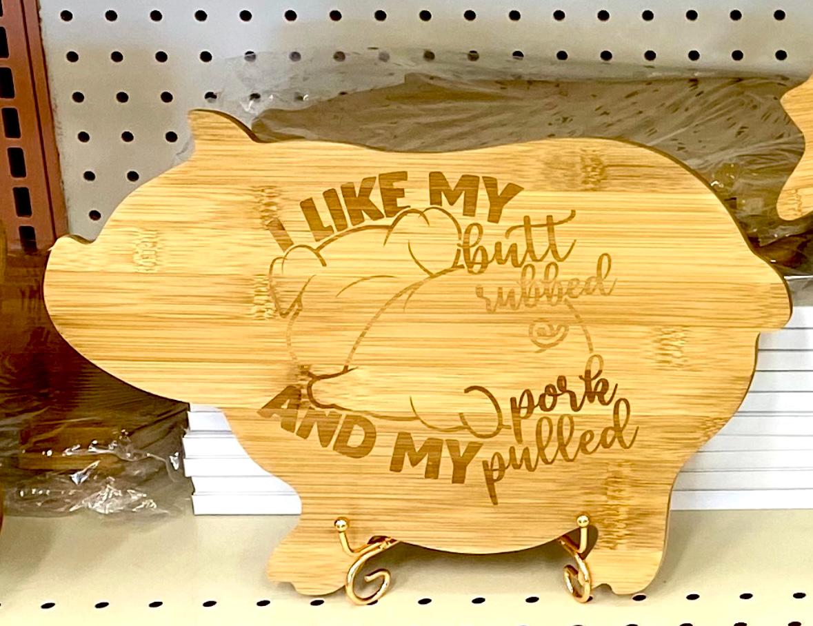 Bamboo pig-shaped cutting board with custom engraving, shown next to kitchen utensils.