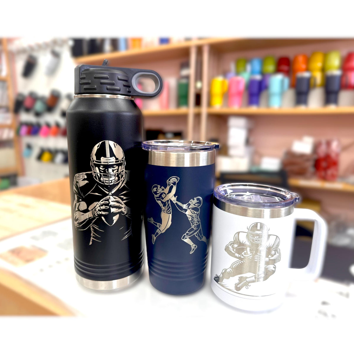 Various sizes and styles of black custom football tumblers, including mugs and water bottles, displayed together.