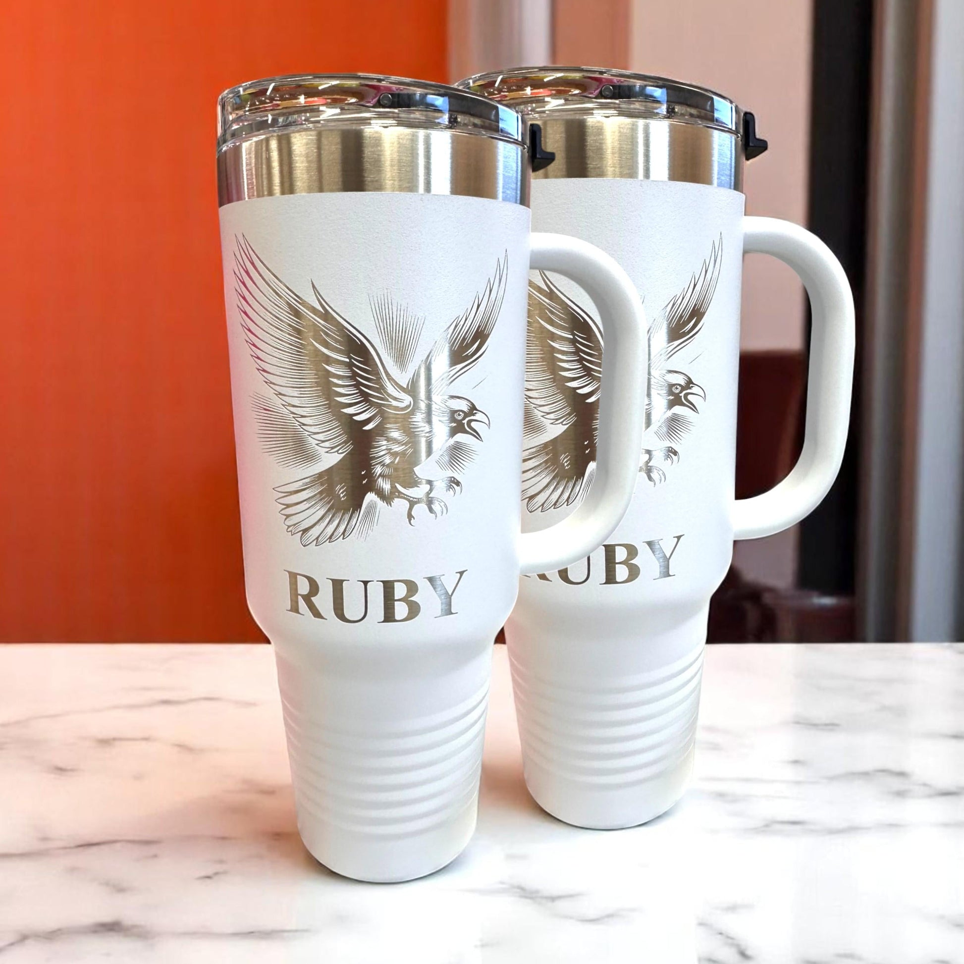 Birn Crow 40 oz Tumbler with Handle. Stainless steel tumbler with handles. tumblers have a gold eagle design and the word 'RUBY' printed on them.