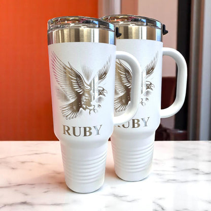 Birn Crow 40 oz Tumbler with Handle. Stainless steel tumbler with handles. tumblers have a gold eagle design and the word 'RUBY' printed on them.