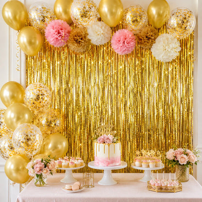 Elegant party backdrop featuring shimmering gold foil fringe curtains, pink and gold latex balloons, and delicate paper pom-poms.