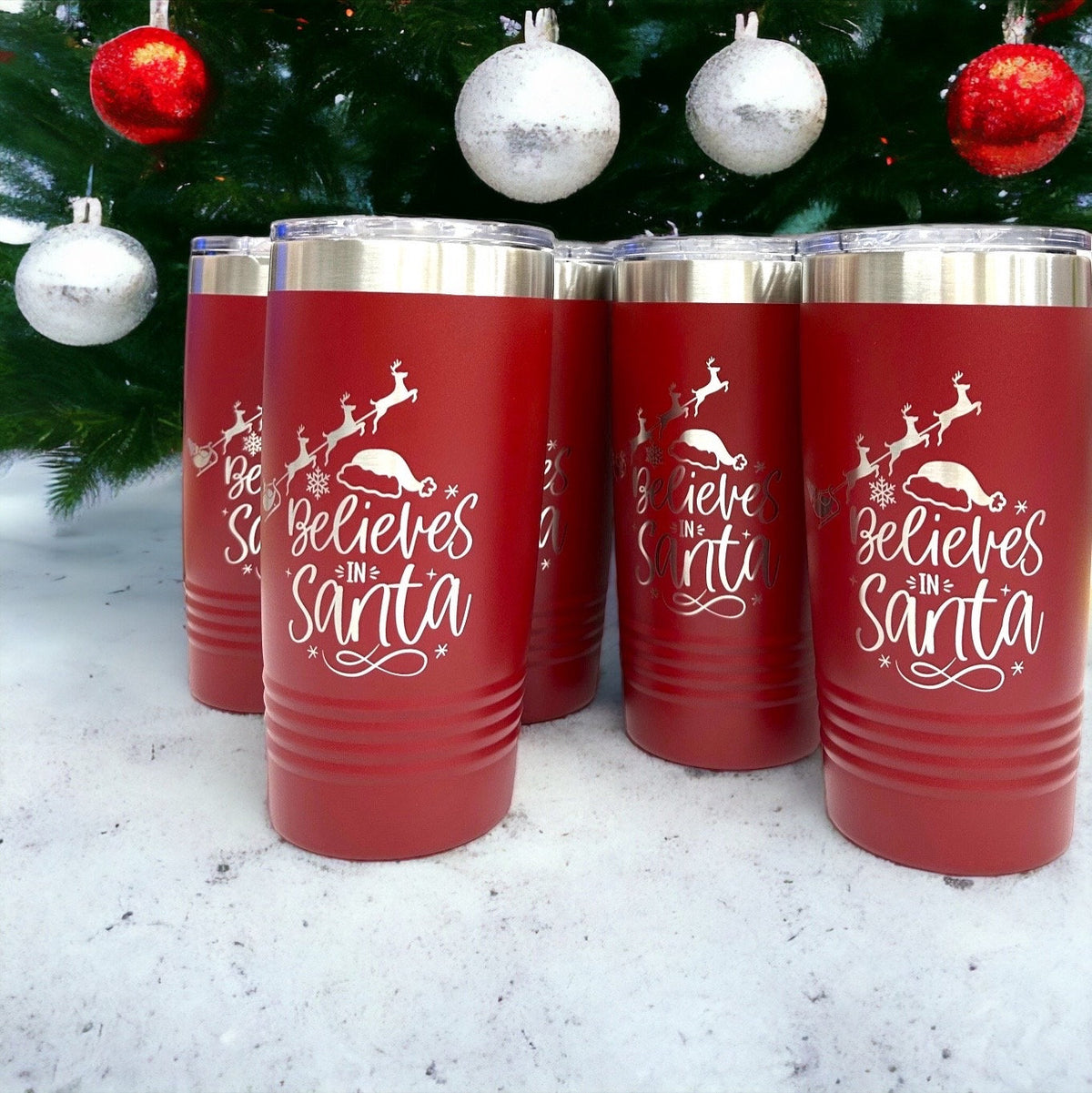 Red stainless steel tumbler with 'Believes in Santa' and reindeer laser engraving, perfect Christmas coffee mug.