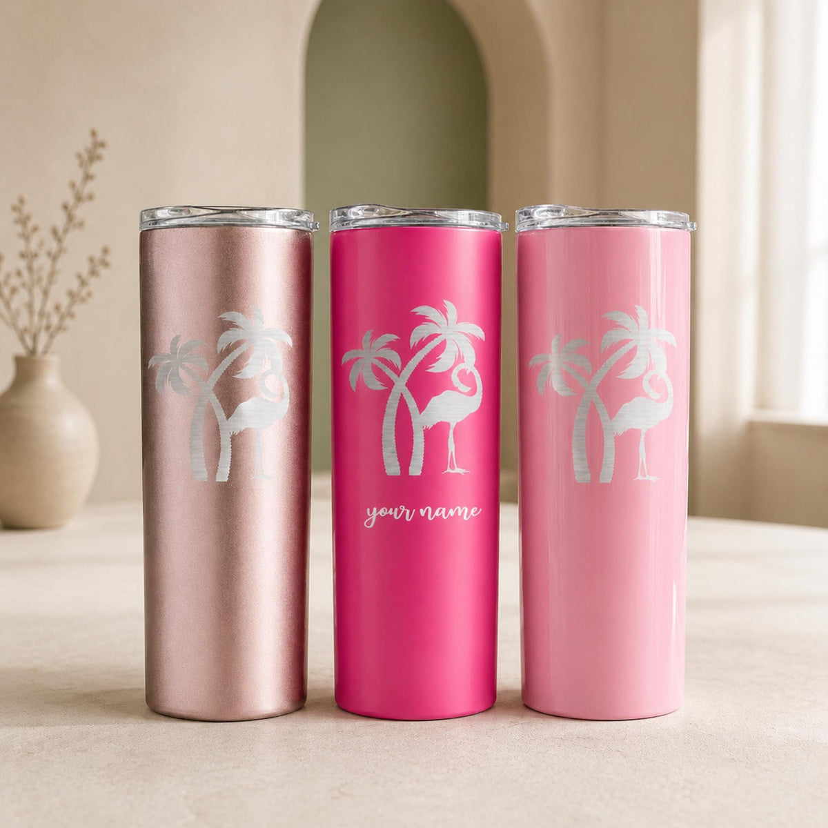 Three personalized flamingo tumblers in rose gold, hot pink, and pastel pink with silver palm artwork.