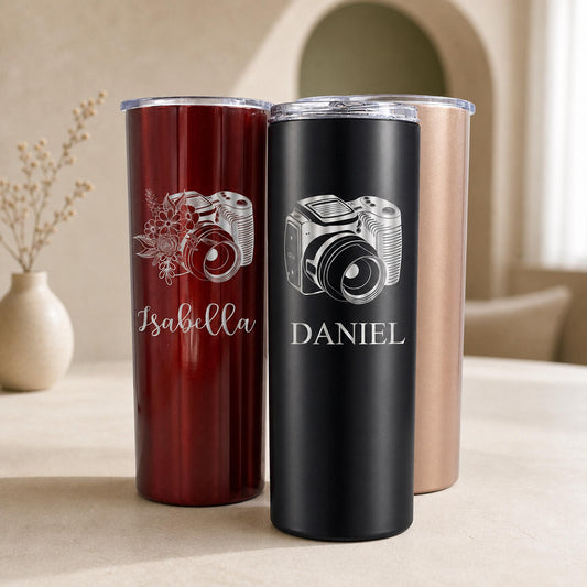 A white photographer tumbler cup with a laser-engraved camera lens design, 20 oz capacity, on a white background.