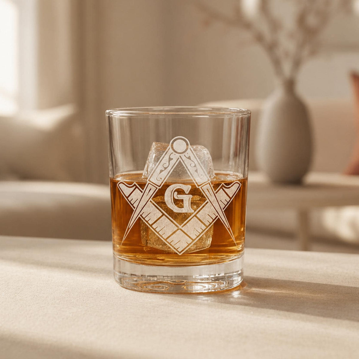 Clear rocks glass with laser-engraved Masonic square and compass symbol, filled with amber whiskey and ice.