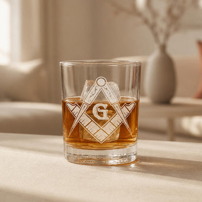 Clear rocks glass with laser-engraved Masonic square and compass symbol, filled with amber whiskey and ice.
