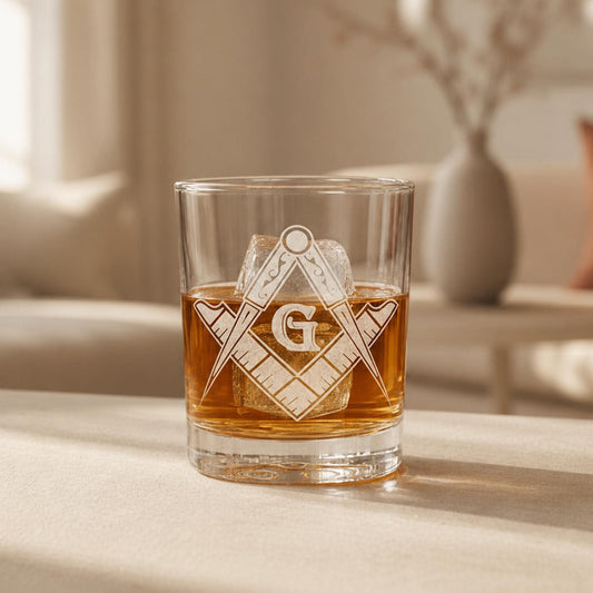 Clear rocks glass with laser-engraved Masonic square and compass symbol, filled with amber whiskey and ice.