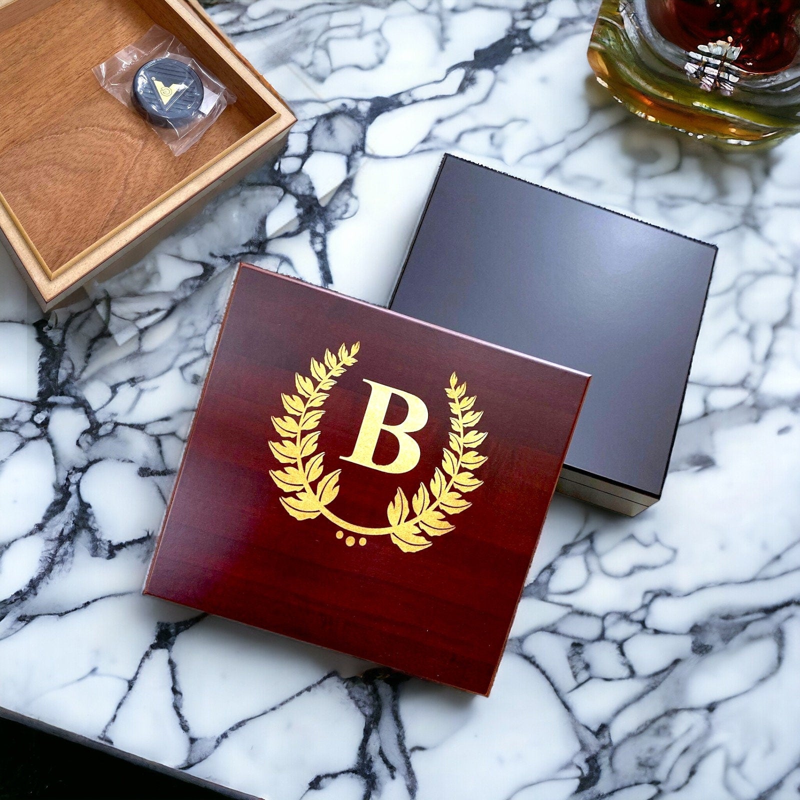 Engraved cherry wood cigar humidor with a custom gold monogram on a polished desktop.