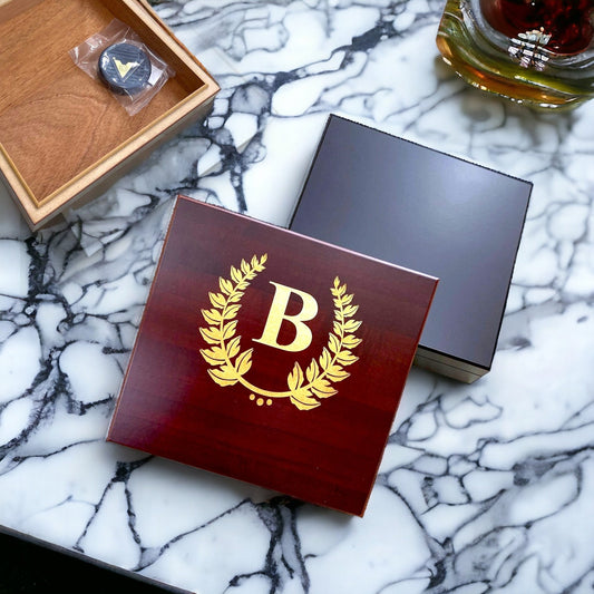 Engraved cherry wood cigar humidor with a custom gold monogram on a polished desktop.