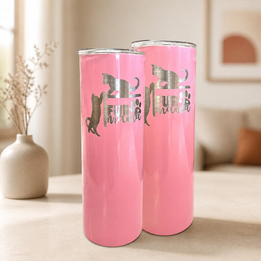 Two pink Fur Mama cat tumblers with silver cat silhouettes and paw-print lettering in a neutral home setting.