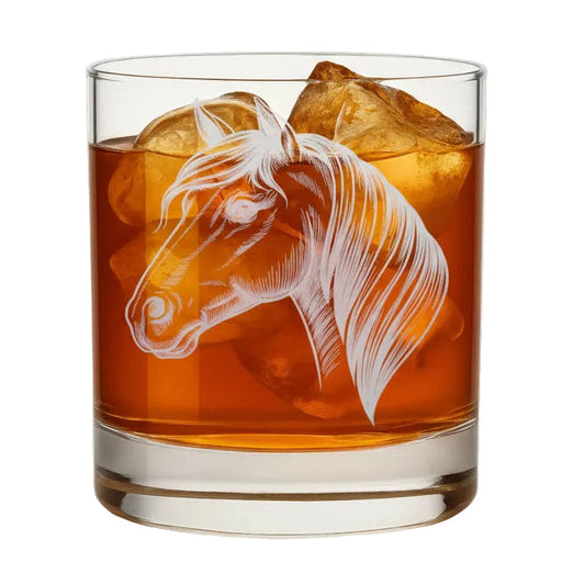 Glass with a horse etching filled with amber liquid and ice cubes on a wooden surface.
