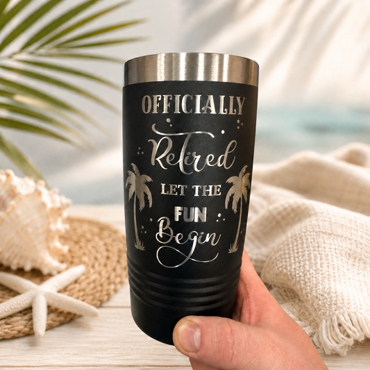 Hand holding engraved Officially Retired stainless steel tumbler in a beach setting