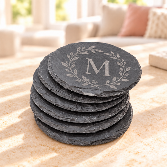 Personalized dark slate coasters with engraved monogram displayed on a table in a bright living room